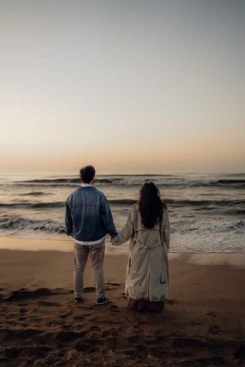 Giovanna ed Enzo di spalle, mano nella mano davanti al mare al tramonto