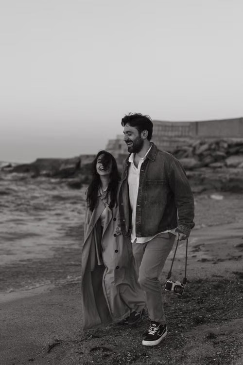 Giovanna ed Enzo camminano ridendo sulla spiaggia, in bianco e nero